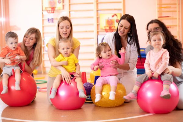 Group of young moms and their babies doing yoga exercises on gymnastic balls at fitness gym
